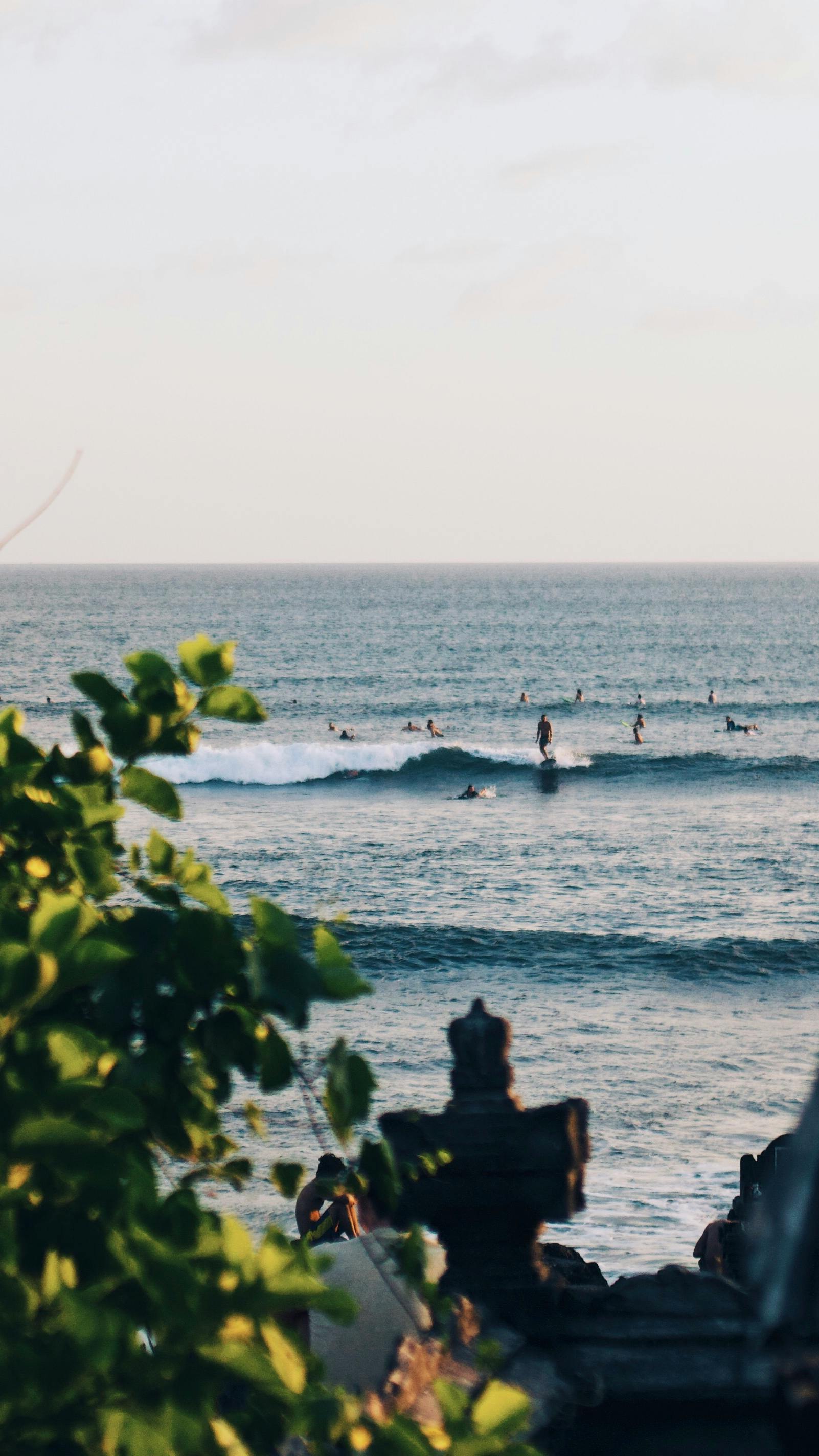 Uluwatu cliffs and temple silhouette at sunset with surfers paddling out below the limestone walls in southern Bali