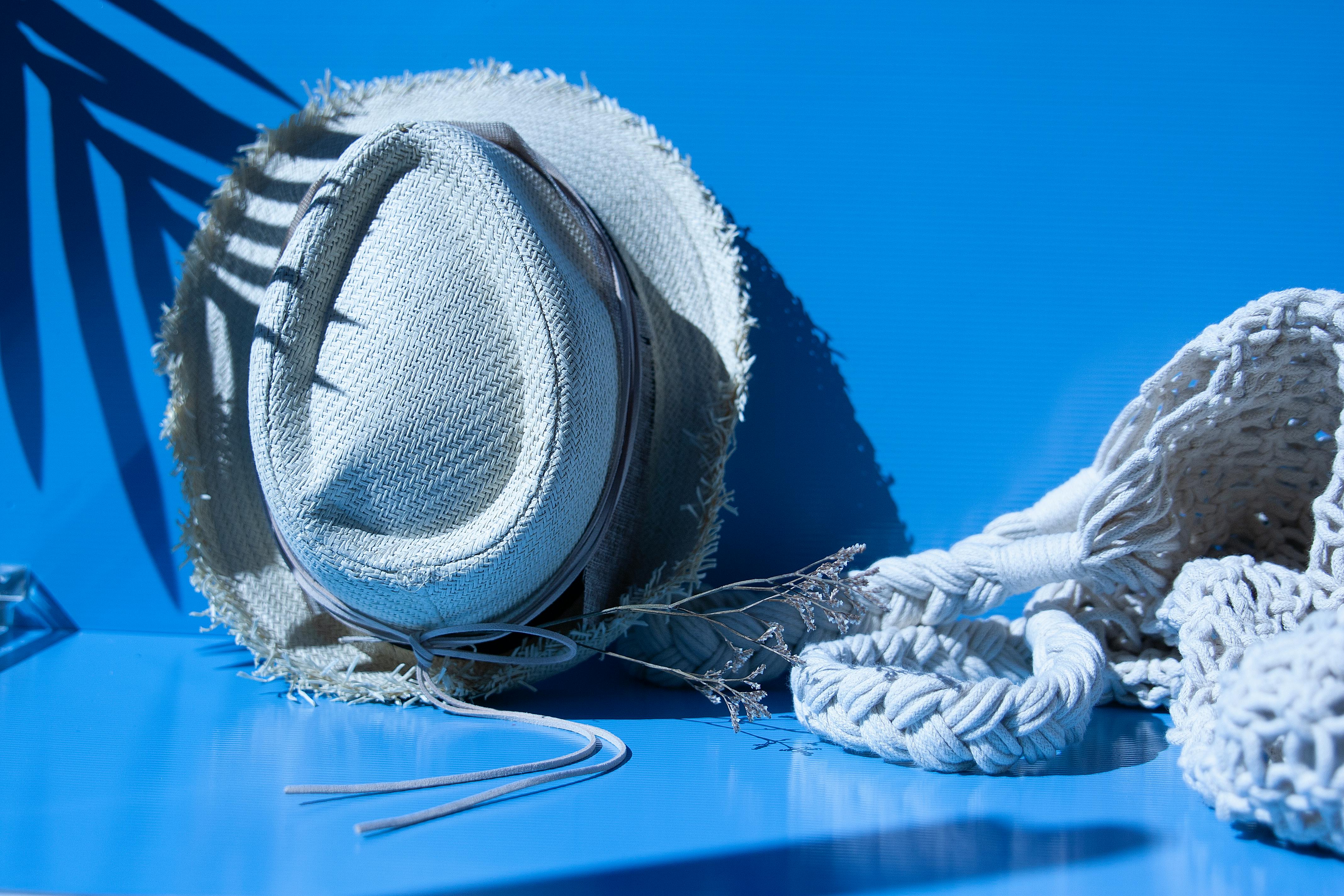 Chic straw hat and macrame bag on vibrant blue backdrop with palm shadows, perfect for summer vibes.