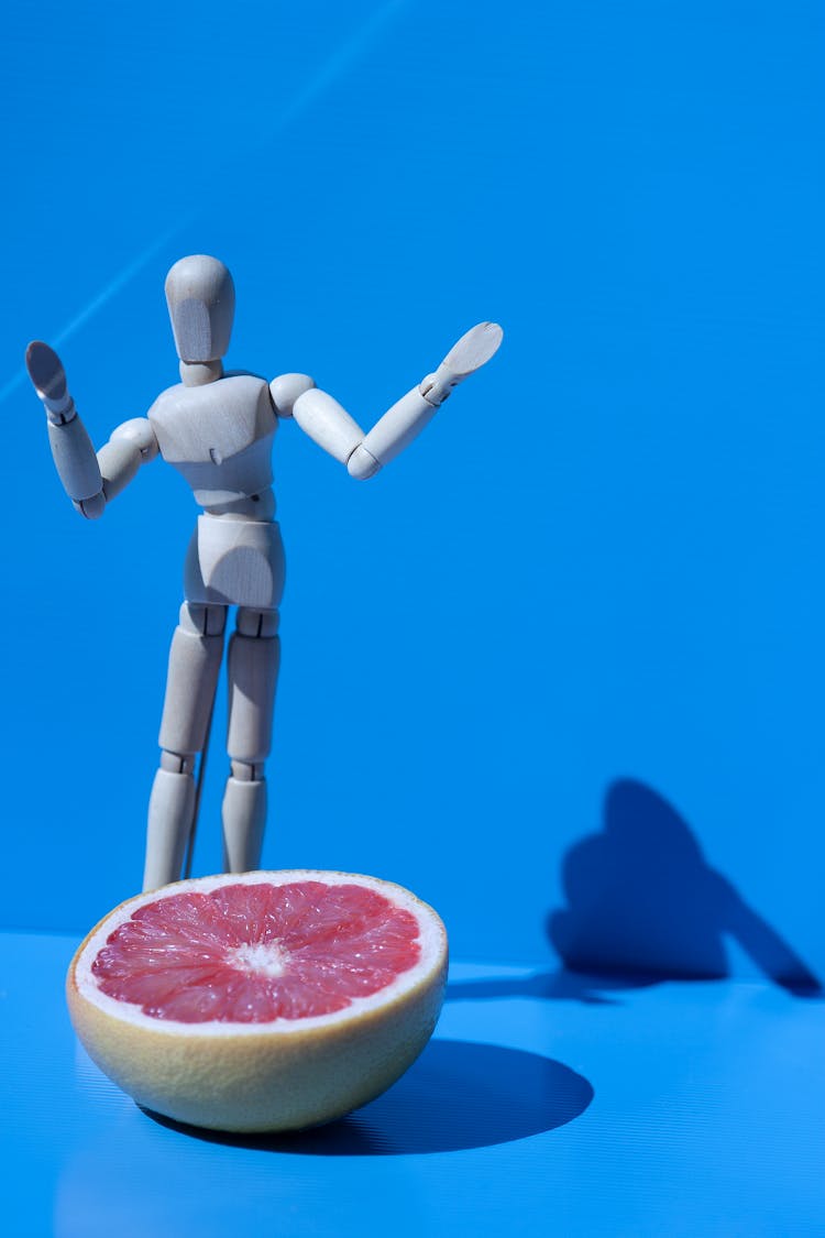 Wooden Drawing Mannequin And A Grapefruit On Blue Background