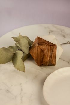 A minimalist still life featuring a wooden geometric object and dried leaves on a marble surface.