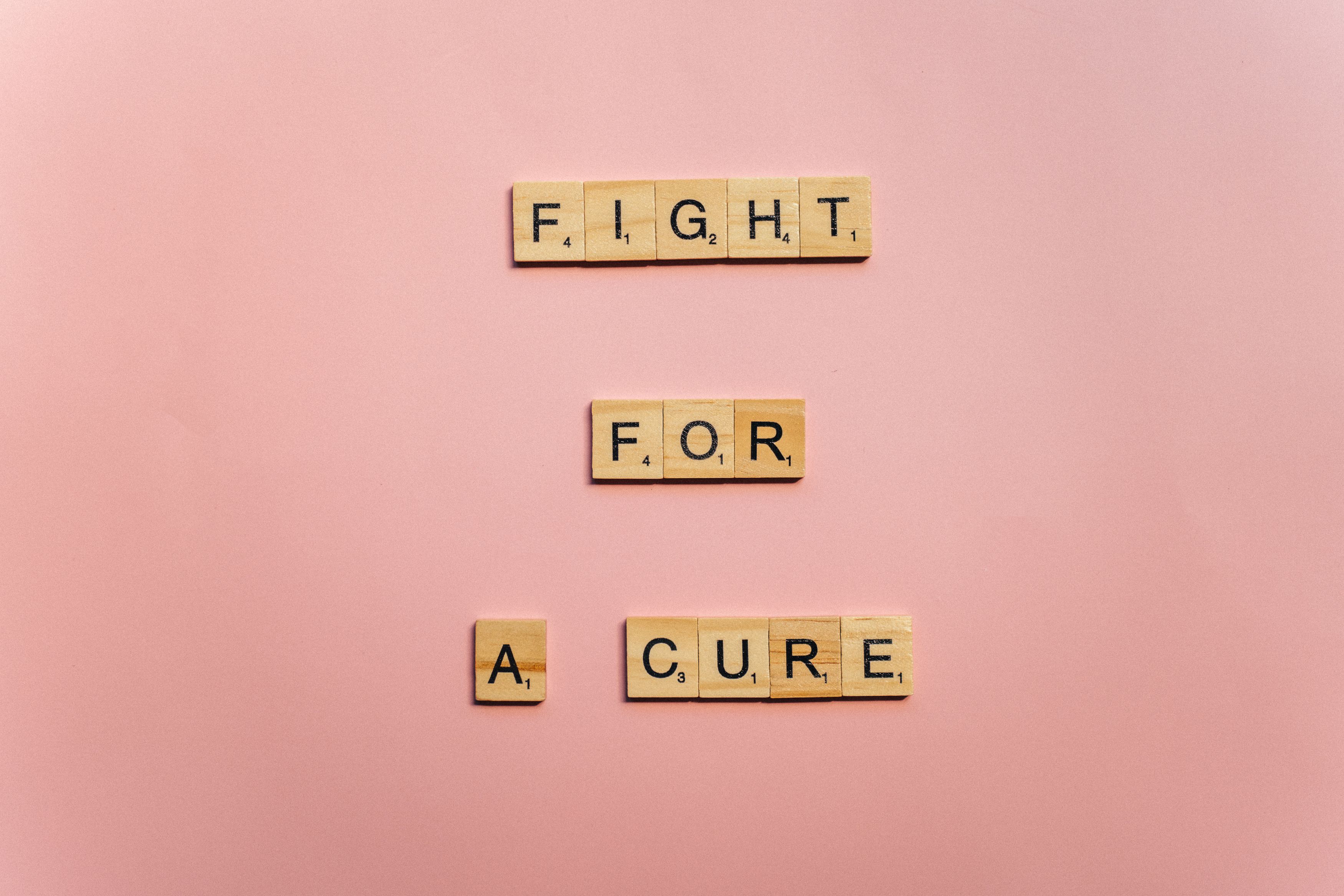 Wooden letter tiles on a pink background spell 'Fight for a Cure'. Motivational design.