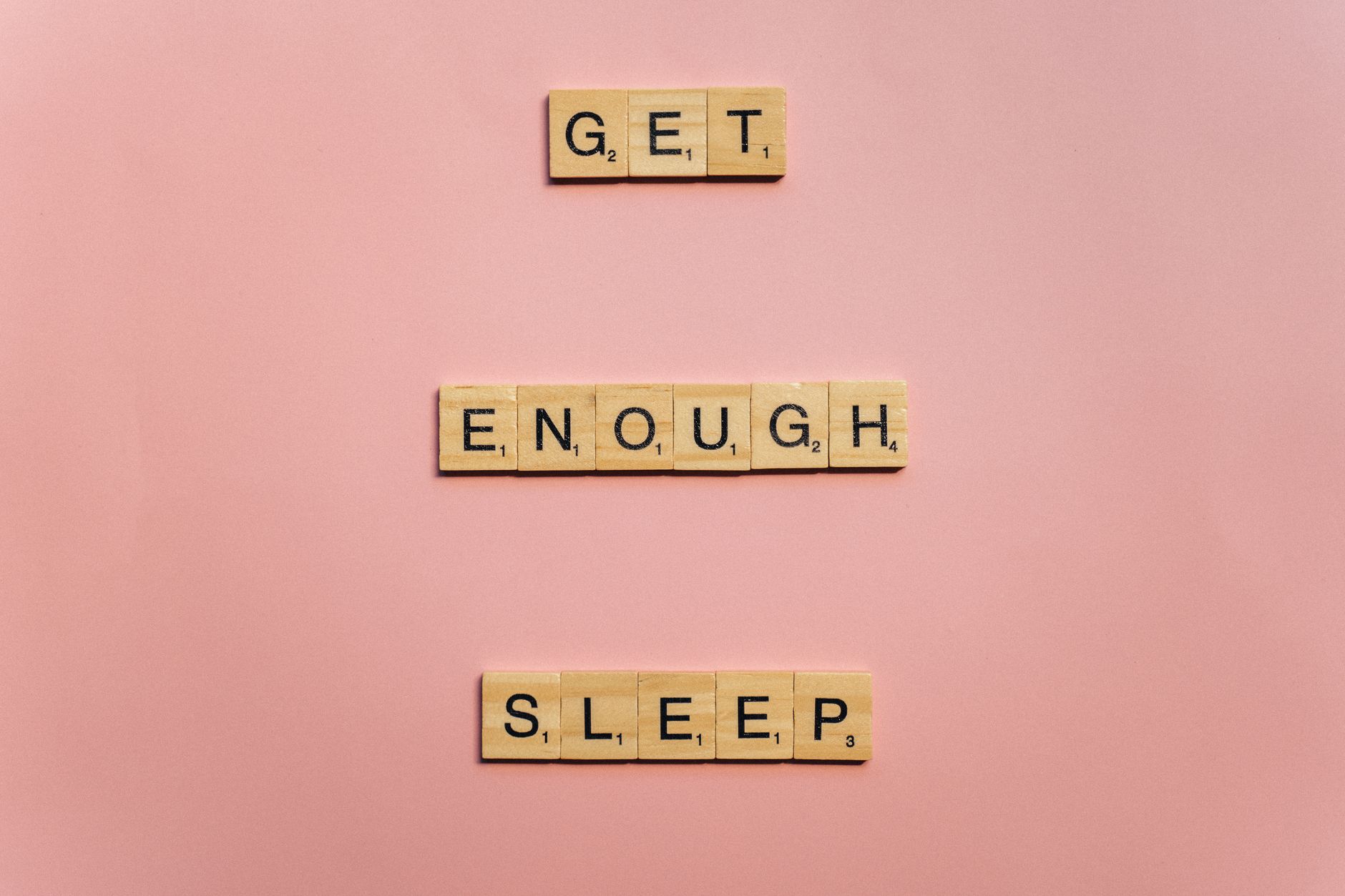 Scrabble tiles on a pink background spelling out 'Get Enough Sleep'. Ideal for wellness and lifestyle themes.