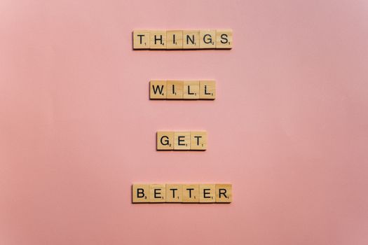 Inspirational words 'Things will get better' arranged in Scrabble tiles against a pink backdrop.