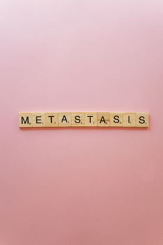 The word 'Metastasis' spelled with scrabble tiles on a pink background, symbolizing cancer and disease.