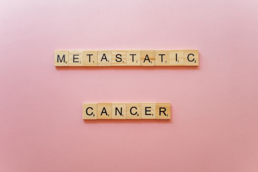 Scrabble tiles spell 'Metastatic Cancer' on pink background, symbolizing awareness.