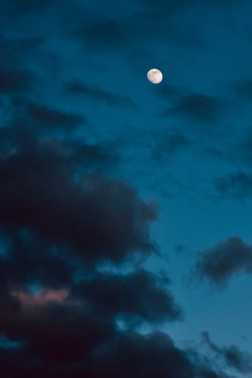 Free From below of bright moon with craters shining in dark cloudy sky in evening Stock Photo