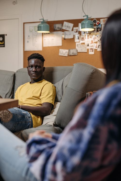 Free African American man in a yellow shirt having a conversation on a sofa at home. Stock Photo