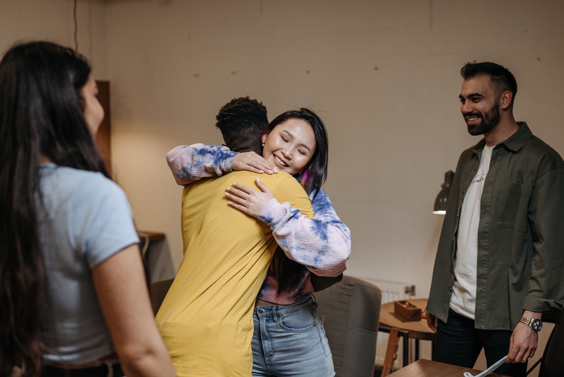 A joyful gathering of diverse friends hugging indoors, radiating warmth and friendship.
