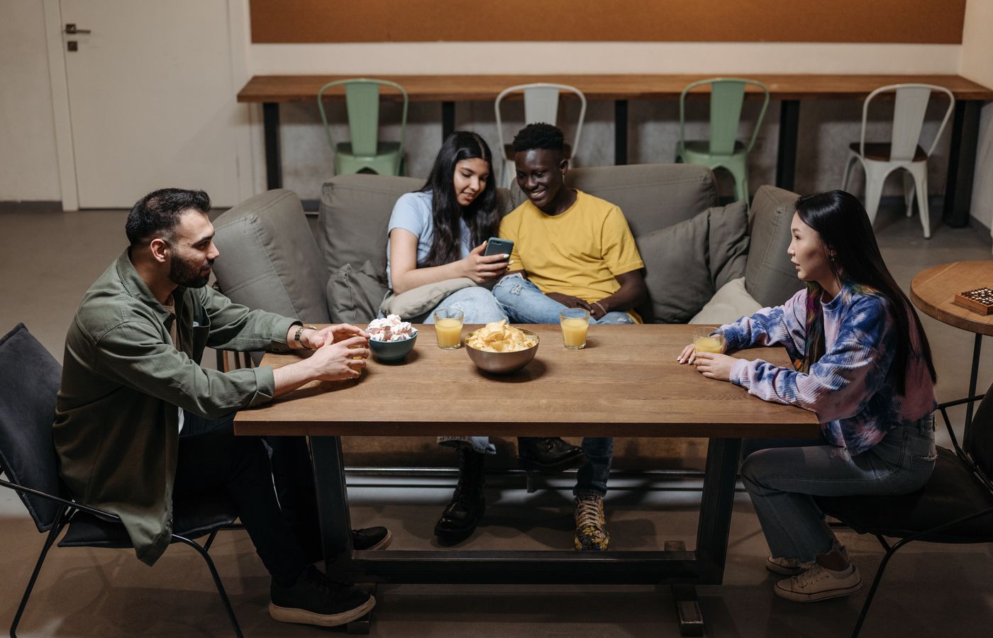 A group of young adults socializing around a table with snacks indoors.
