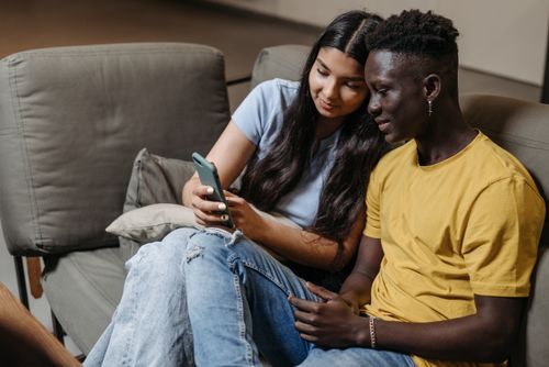 Free A young couple sitting on a couch, looking at a smartphone together, indoors. Stock Photo