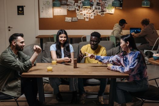 A diverse group of young adults playing Jenga indoors, having fun and connecting over a board game.