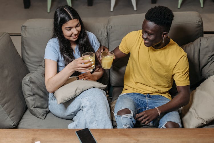 Man And Woman Holding Drinks While Sitting On Sofa