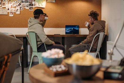 Two men in hoodies enjoying drinks and conversation in an informal office setting.
