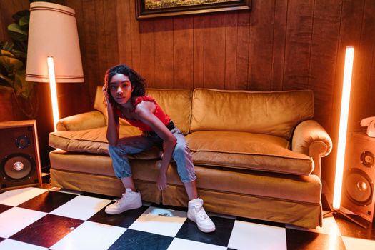 A stylish young adult strikes a pose in a retro-themed living room featuring warm lighting and vintage decor.