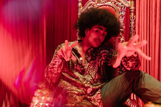 Man in vibrant outfit and afro hairstyle posing in a creative indoor setting.