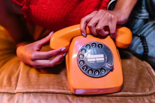 Close-up of a woman holding an orange vintage rotary phone, evoking nostalgia and retro vibes.