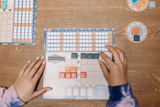 Hands arranging tiles on a strategic board game during a fun game night.