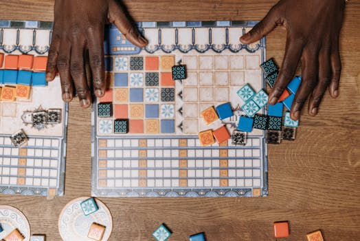 Top view of hands playing a strategic board game with colorful tiles.