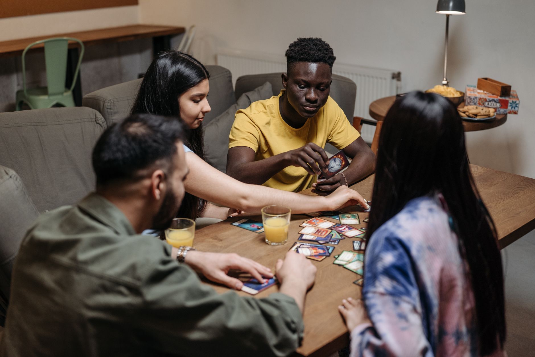 A diverse group of friends playing a strategic card game while enjoying drinks indoors.