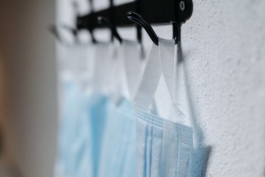 A row of blue protective face masks hanging on wall hooks indoors.