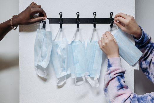 Close-up of hands hanging disposable face masks on wall hooks for safety and organization.