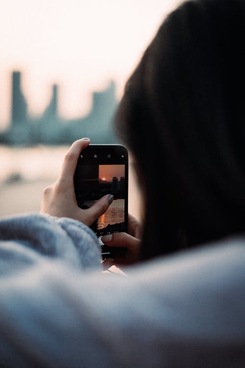 Woman Holding a Cellphone Taking Photo of the City