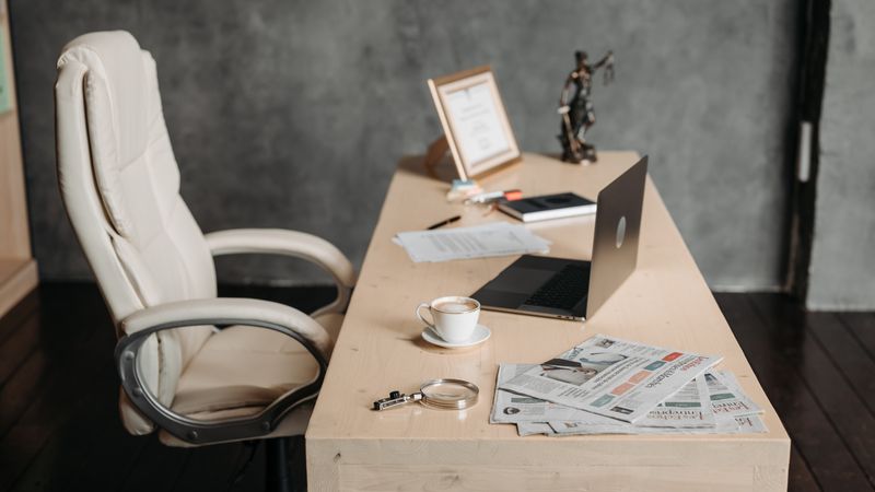 A clean office workspace featuring a cup of coffee, laptop, and newspapers on a wooden desk for a productive environment.