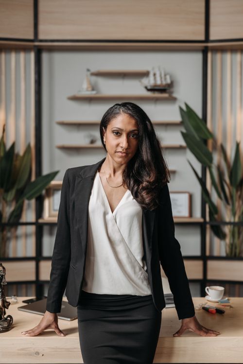 Free Confident businesswoman in black suit posing at her desk in a modern office space. Stock Photo
