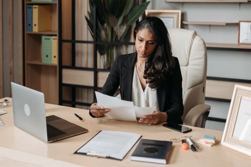 Free Business woman focused on paperwork at office desk, reviewing documents. Stock Photo