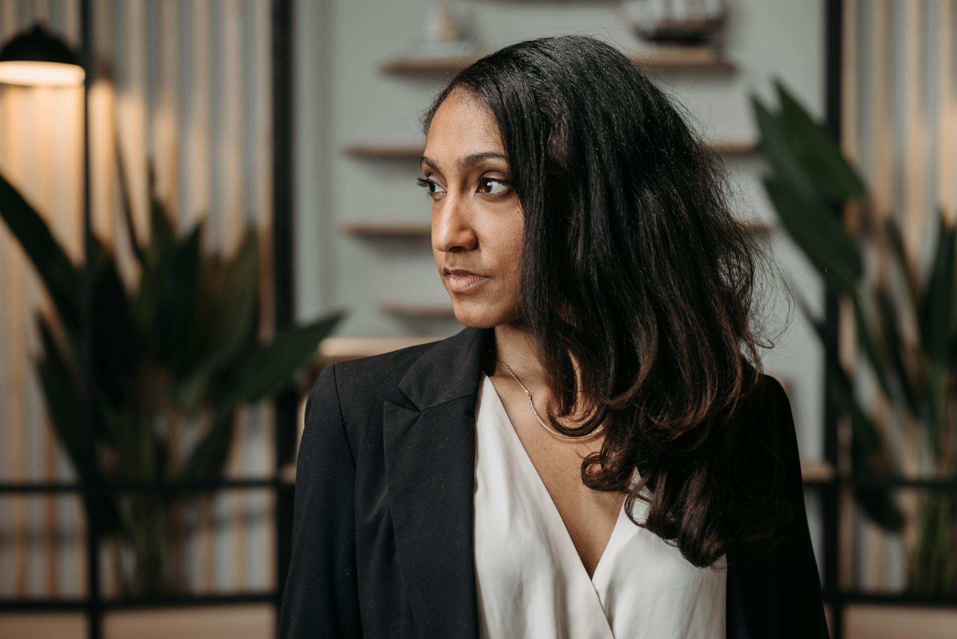 Confident woman in business attire looking away indoors. Stylish and professional setting.