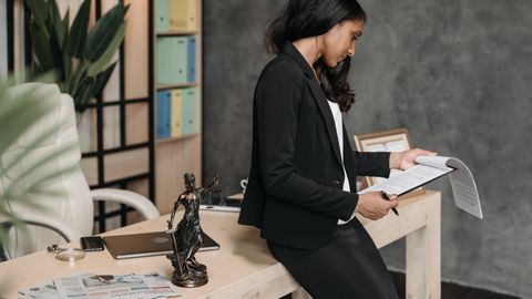 A professional woman in a business suit reviews legal documents at her office desk.