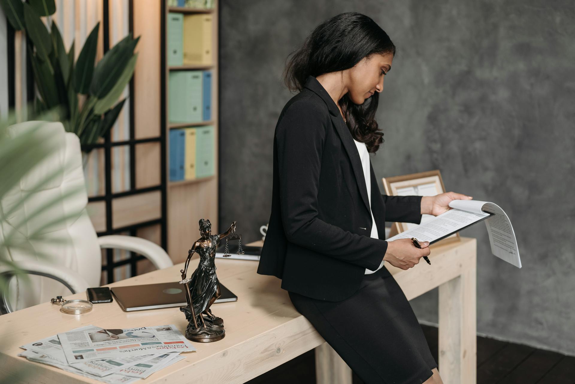 A professional woman in a business suit reviews legal documents at her office desk.