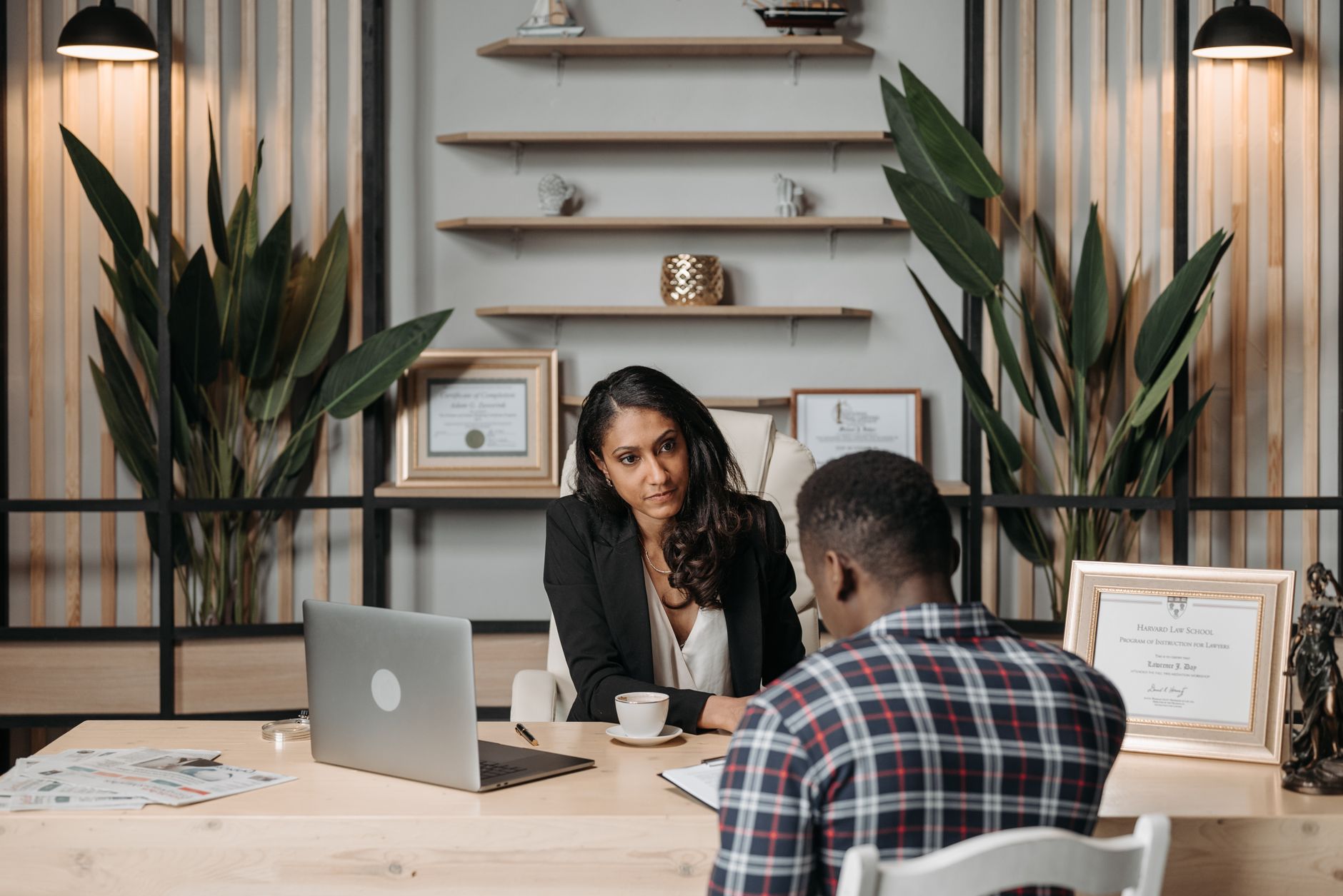 Two professionals engaged in discussion in a modern office with certificates and plants.