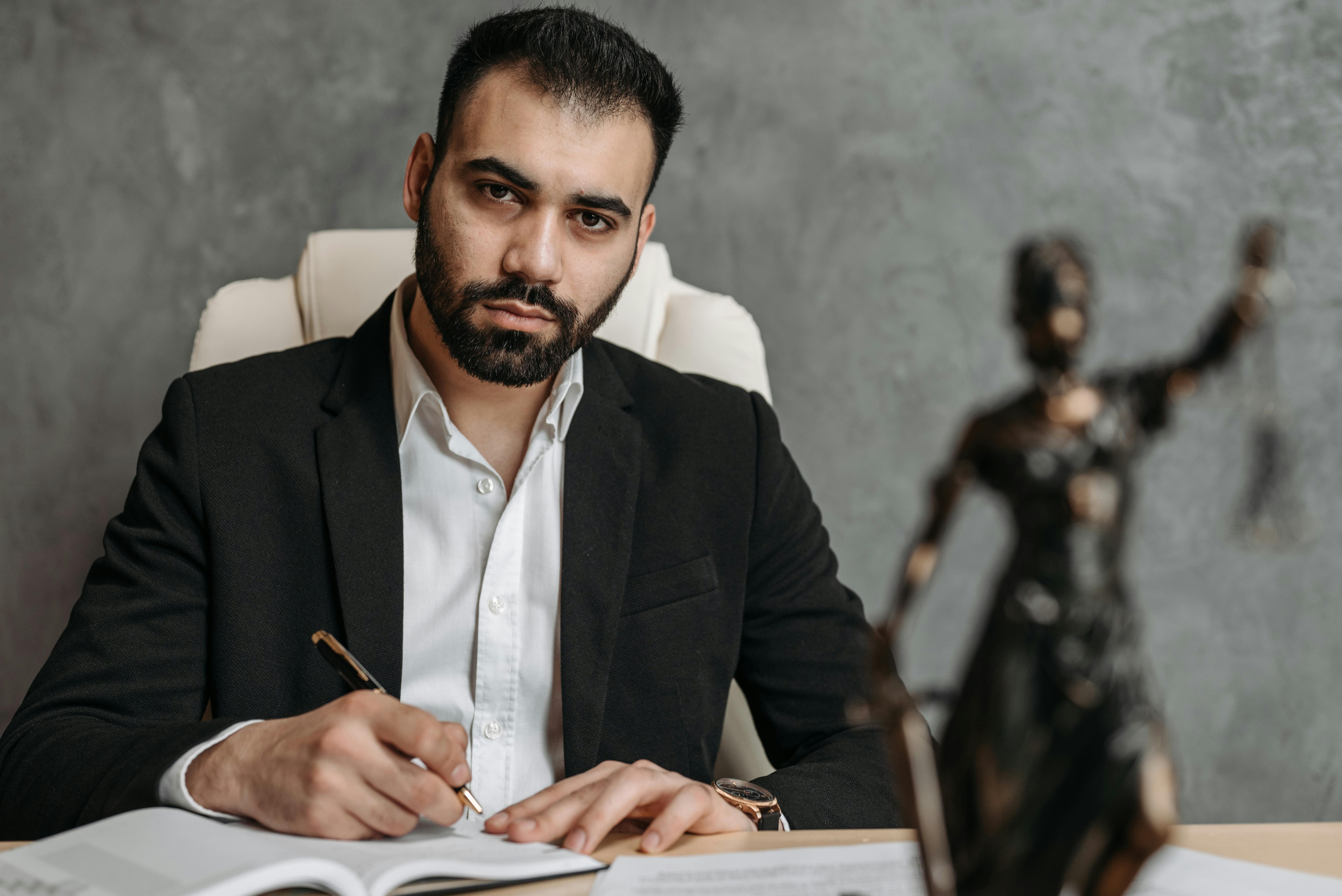 A serious lawyer in a black suit working diligently at his office desk.