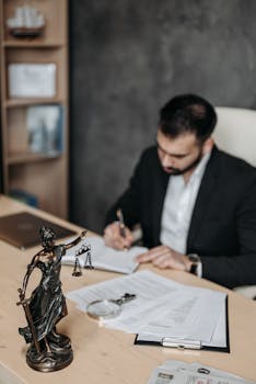 A lawyer concentrates on paperwork in an office; legal statue visible on desk.