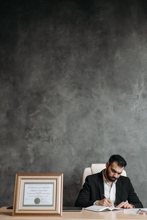 Free An adult man focused on writing at his office desk with framed certificate and ample copy space. Stock Photo