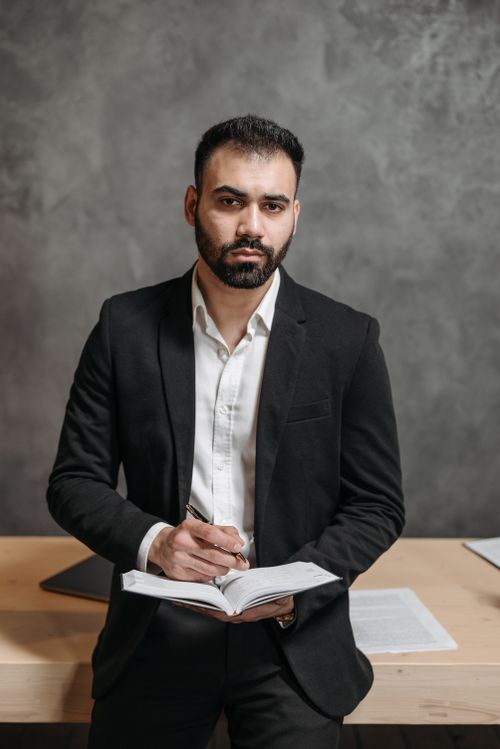 Free Businessman with a beard holding a notebook and pen in a formal office setting Stock Photo