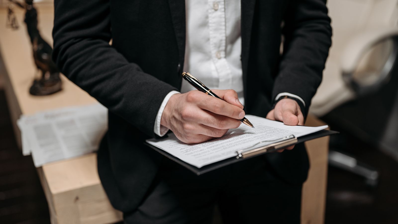 Business professional signing a contract on a clipboard at the office.