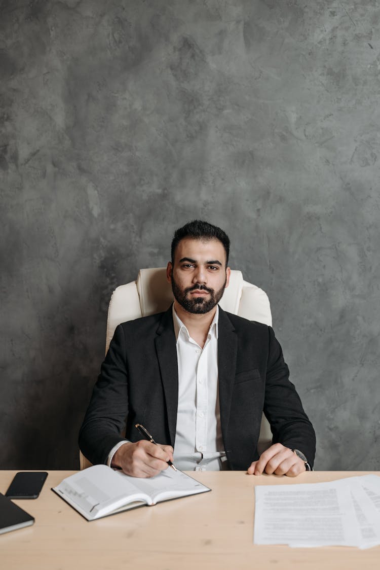 A Man In Black Suit Sitting On White Chair