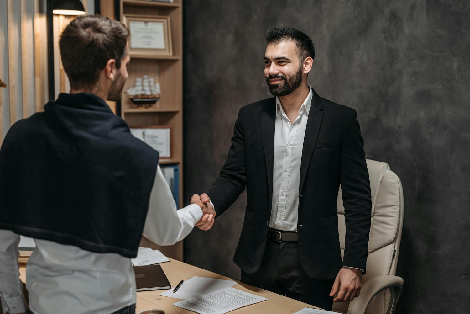 Two businessmen shaking hands in a modern office, sealing a business deal.