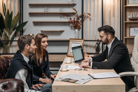 Three professionals engaged in a business discussion at an office desk with a laptop.