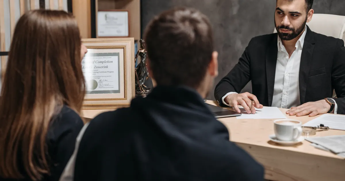 Two clients facing a lawyer in a suit at a desk in an office, seen from behind, representing Take It Down Act enforcement date 2026