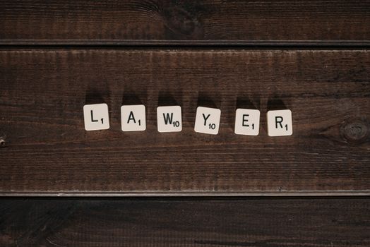 Close-up of scrabble tiles spelling 'lawyer' on a dark wooden surface.