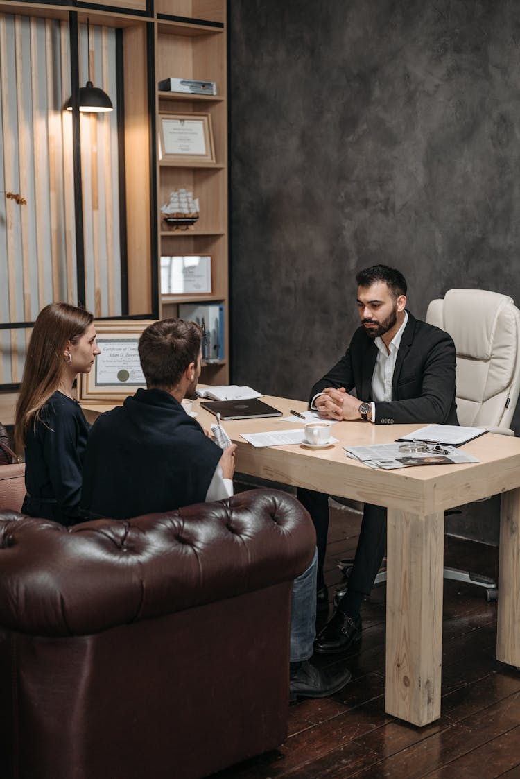 A Man In Black Suit Talking To His Client Sitting On The Couch