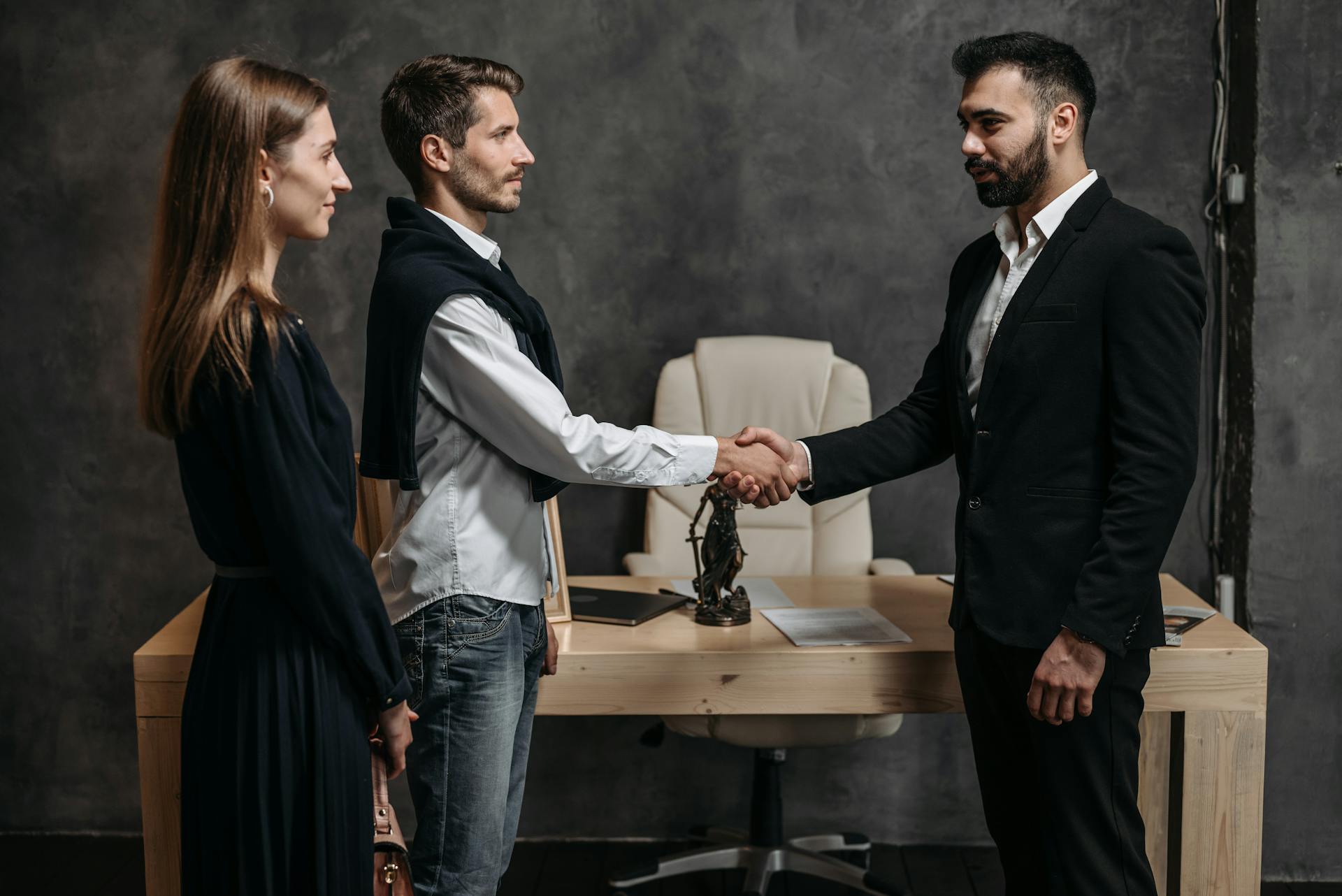 Three business professionals engage in a formal handshake in a modern office setting.