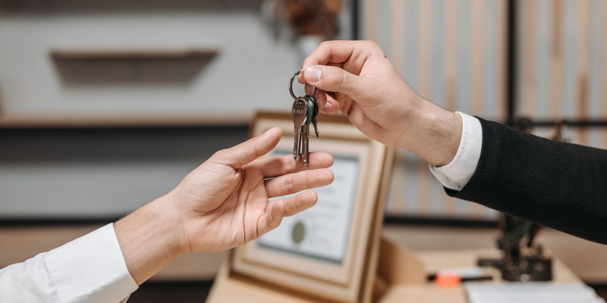 Detailed view of hands exchanging keys in a professional office environment, symbolizing real estate or business transactions.