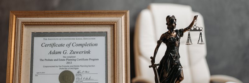 A framed legal certificate and Lady Justice figurine on a desk in a law office setting.