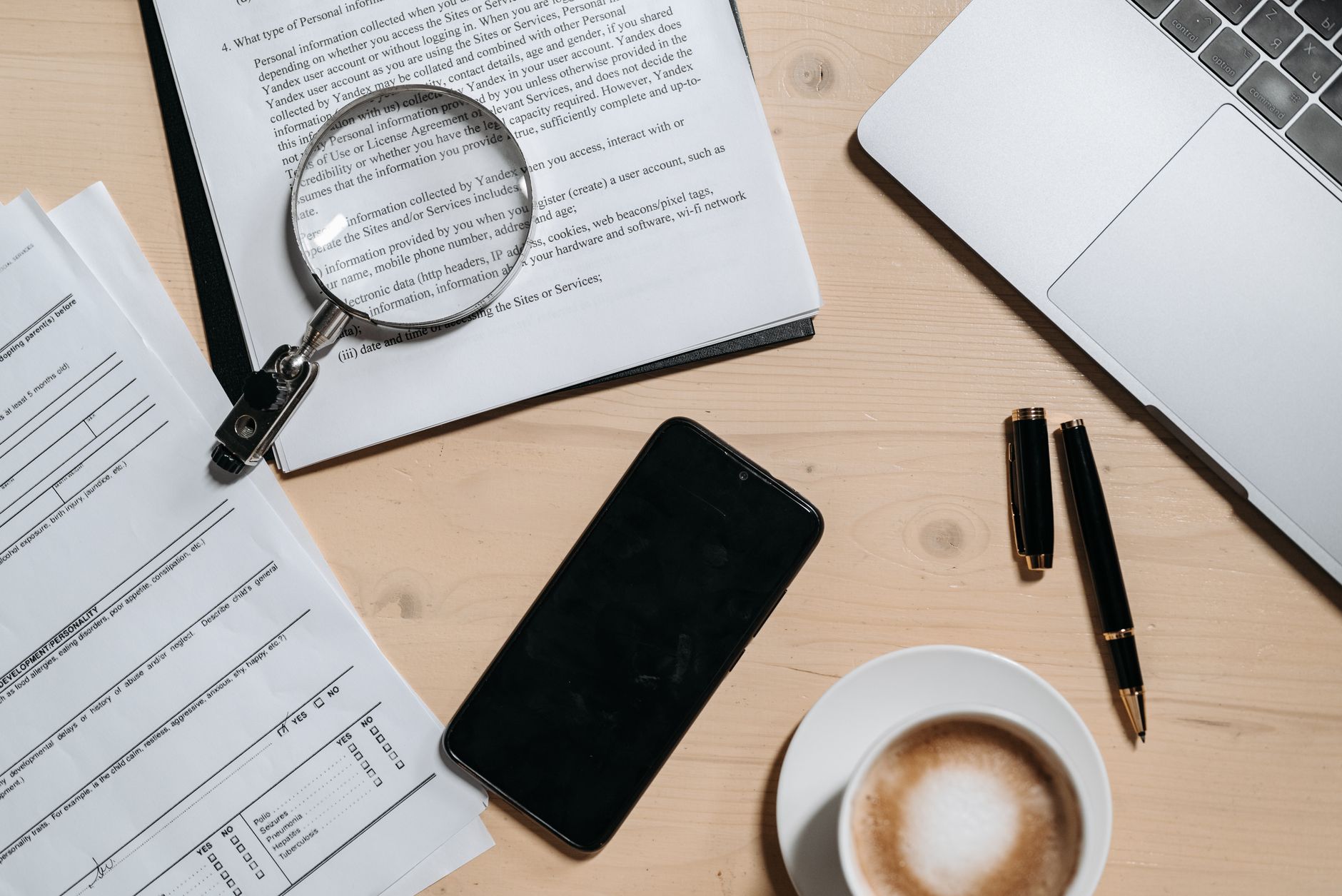 Top view of documents, laptop, coffee, and magnifying glass on office desk.