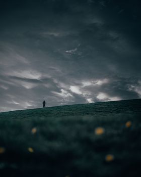 A solitary person stands against a dramatic sky on a hill in Ottawa, Canada, conveying solitude and vastness.