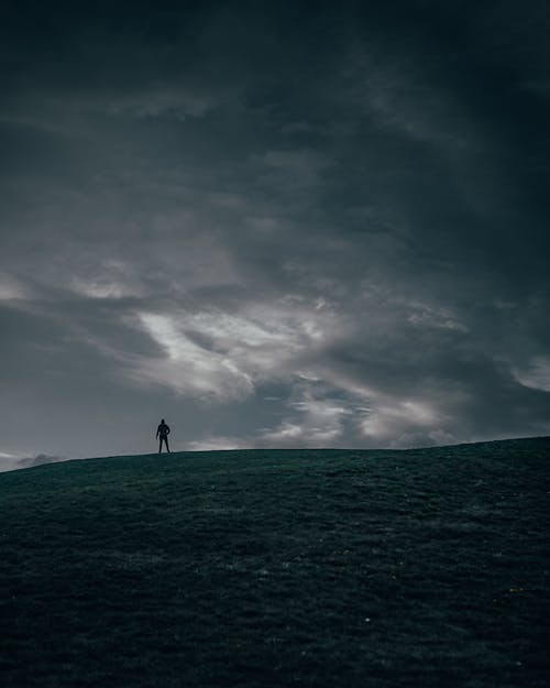 Silhouette of Person Standing on Green Grass Field Under Cloudy Sky